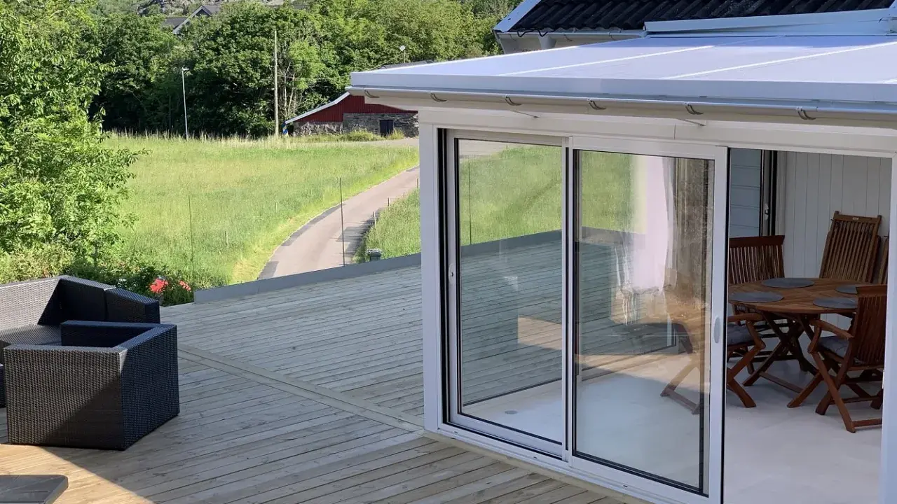 Nybyggd veranda med glaspartier och tak, perfekt för att bygga en mysig uteplats. Utsikt över grönskande landskap.