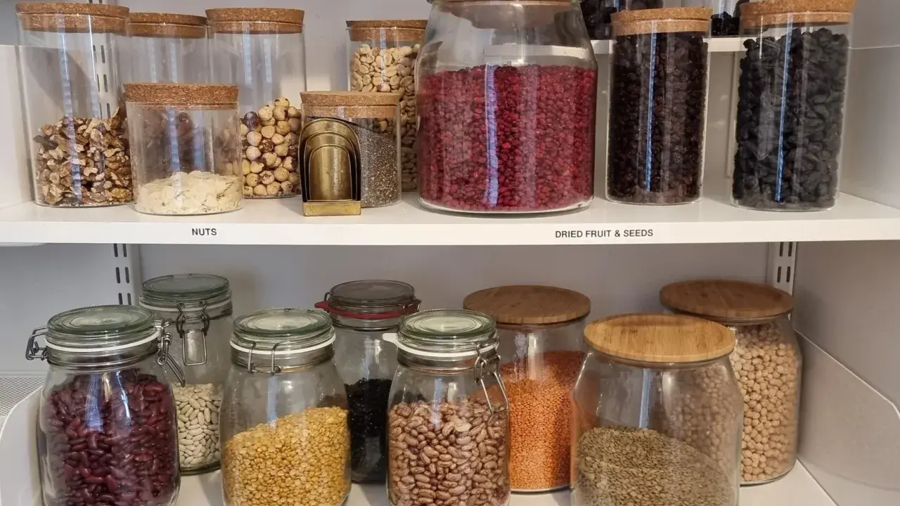 Välordnat skafferi med glasburkar fyllda med nötter, torkad frukt, frön och baljväxter. Perfekt för att organisera skafferi.