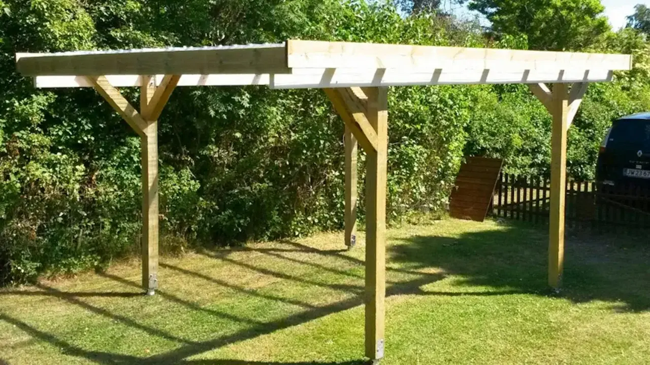 En nybyggd carport på plintar står på en gräsmatta. Träkonstruktionen har ett tak av plast eller metall.