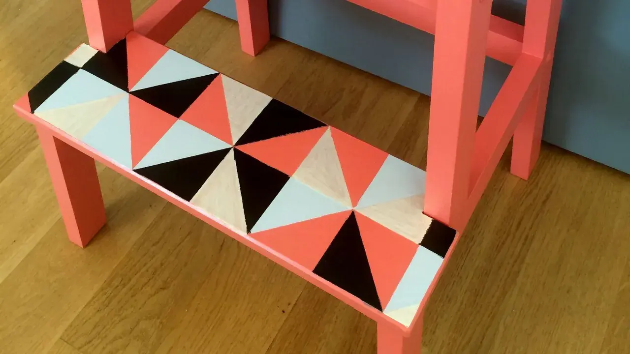 En pall med geometriskt mönster i orange, svart, vitt och ljusblått. Ett kreativt sätt att måla pall!