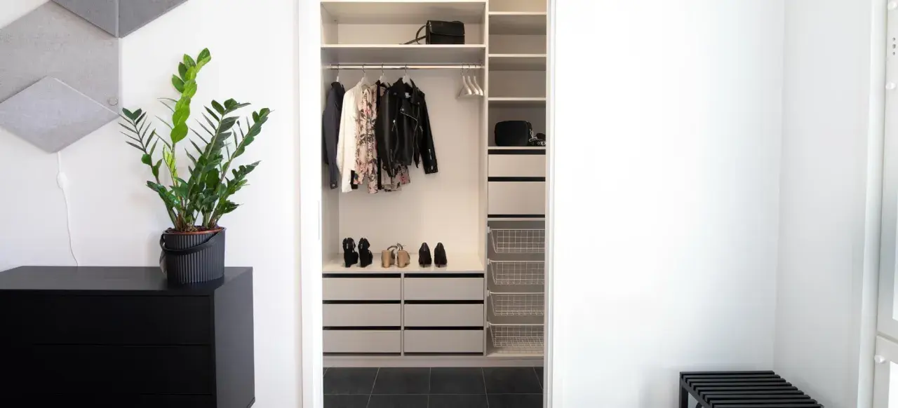 En stilren liten walk in closet med kläder, skor och väskor. En grön växt på en svart byrå ger liv.
