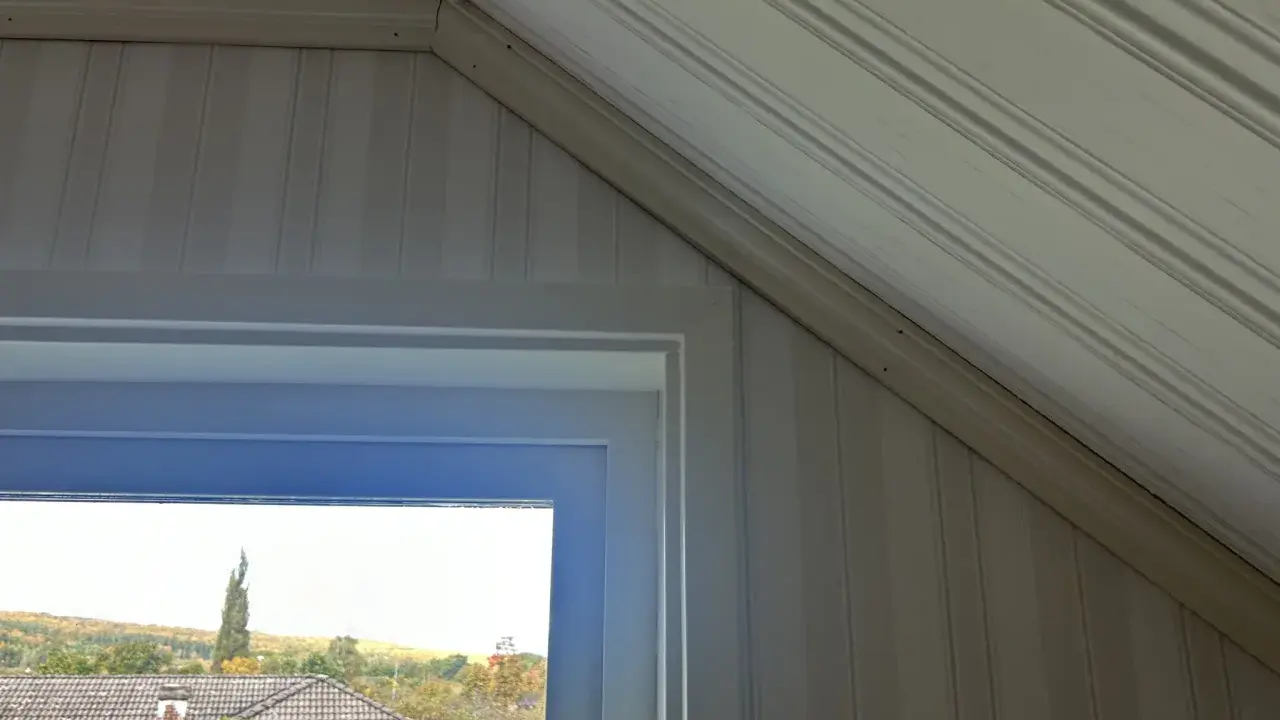 Takskena i snedtak med panelklädda väggar. Fönstret ger utsikt över hus och höstfärgad natur.
