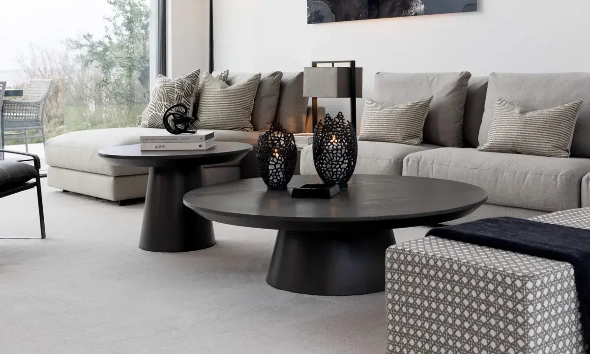 Ett modernt vardagsrum med en stor, mörk soffa och ett elegant, runt soffbord. Två svarta ljuslyktor står på soffbordet.