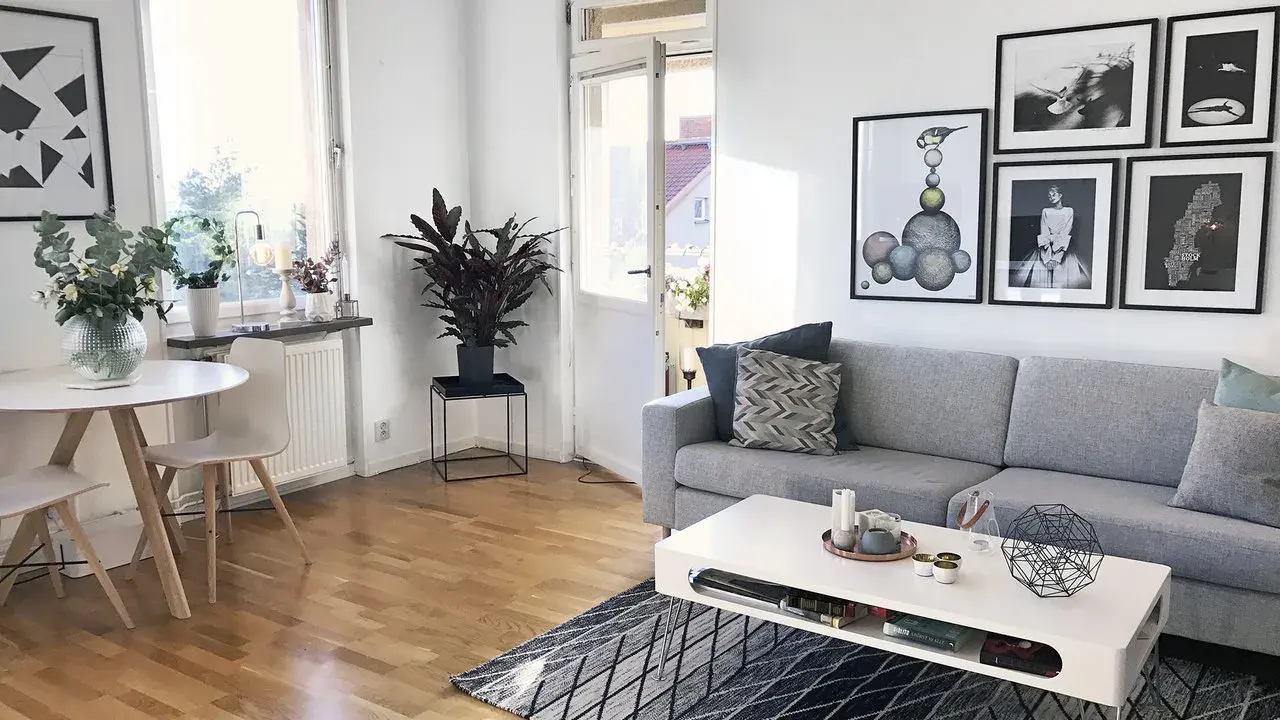 Mysig etta med grå soffa, vitt soffbord och en rund matplats. Konst på väggarna ger personlighet.
