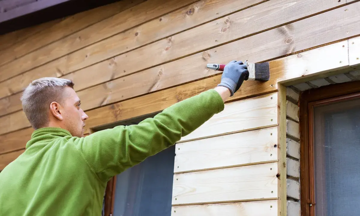 Man målar panel utomhus med pensel. Träet får en varmare ton.