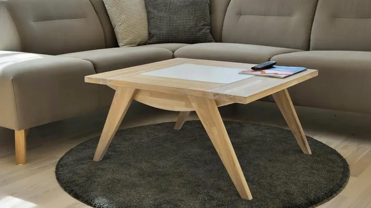 Ett smart soffbord i ljust trä med en vit inläggning, placerat på en rund, mörk matta framför en beige hörnsoffa.
