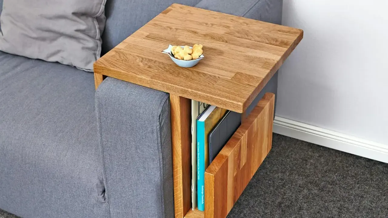 Ett smart diy soffbord i trä som hängs över armstödet på en grå soffa. Perfekt för att förvara böcker och ha en skål med kex nära till hands.
