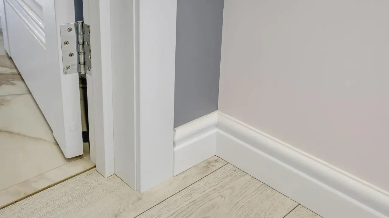 Nymålade vita snickerier runt en dörröppning och längs väggen. Golvet är ljust träliknande laminat.