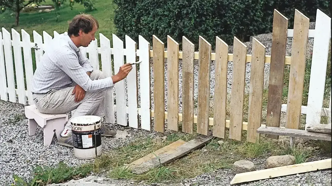 Man målar ett vitt staket. En burk med färg står bredvid.