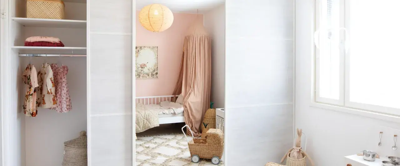 A child's closet with clothes and baskets, a pink bedroom with a bed and canopy, and a white wall with a window.