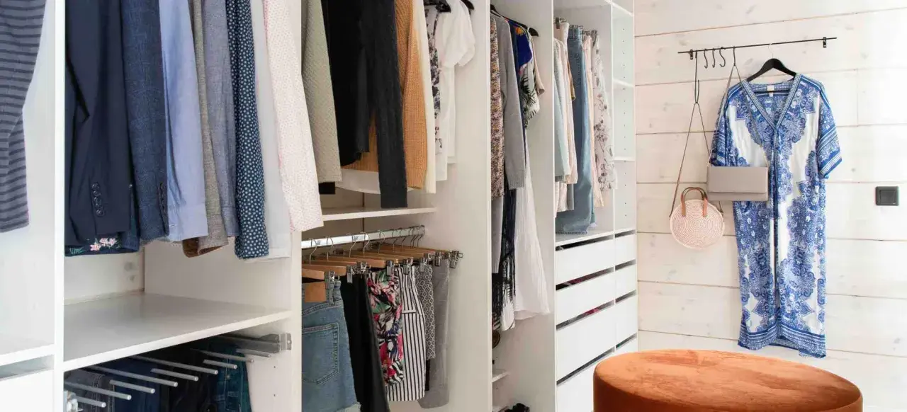 En walk-in closet med kläder på galgar, lådor och en blåvit klänning på väggen.