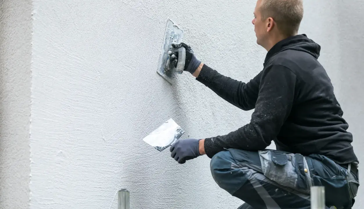 Man putsar en vit fasad med en bredspackel. Det är viktigt att man målar putsad fasad för att skydda den.