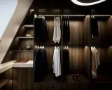 Elegant platsbyggd walk in closet i mörkt trä med stilfull belysning. Hängande kostymer, skjortor och accessoarer.