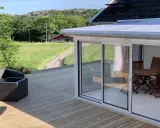 Nybyggd veranda med glaspartier och tak, perfekt för att bygga en mysig uteplats. Utsikt över grönskande landskap.
