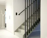 En modern hall med en stilren, målad trappa i ljusa färger och mörka vertikala räcken.