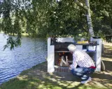 Man tänder en murad grill vid en sjö.