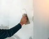 Handen sprider spackel på en vägg med en bredspackel. Arbetet med att måla på spackel fortsätter för att skapa en jämn yta.
