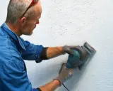 Man slipar en vägg med en excenterslip för att få bort slipdamm innan målning.