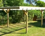 En nybyggd carport på plintar står på en gräsmatta. Träkonstruktionen har ett tak av plast eller metall.