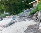 En vacker uteplats sten med grusgångar, stenmurar och en trappa som leder upp mot ett hus.