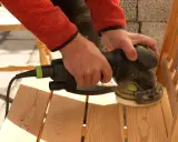 Förbereder för att måla stolar. Händer slipar en trästol med en excenterslip för att få en jämn yta.