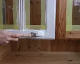 En hand målar en vit ram på en furumöbel. Maskeringstejp skyddar träet.