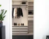 En stilren liten walk in closet med kläder, skor och väskor. En grön växt på en svart byrå ger liv.