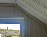 Takskena i snedtak med panelklädda väggar. Fönstret ger utsikt över hus och höstfärgad natur.