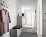 En smal hall med en rosa kappa och en vit halsduk på krokar. En grå förvaringsmöbel med en fårskinnspläd.