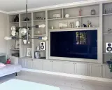 En platsbyggd bokhylla i vardagsrummet med en stor TV i mitten. Hyllorna är fyllda med böcker, dekorationer och växter.