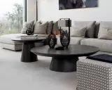 Ett modernt vardagsrum med en stor, mörk soffa och ett elegant, runt soffbord. Två svarta ljuslyktor står på soffbordet.