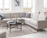 Ljusbeige hörnsoffor i ett modernt vardagsrum med ett runt soffbord, en matta och stora fönster.