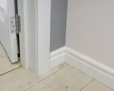 Nymålade vita snickerier runt en dörröppning och längs väggen. Golvet är ljust träliknande laminat.