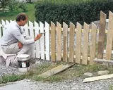 Man målar ett vitt staket. En burk med färg står bredvid.