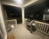 En gasolgrill under taket på altanen, redo för grillkvällar. Bredvid står en gasoltub och ett par skor.