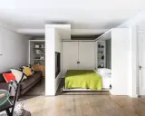 En smart säng i vardagsrummet som fälls ner från väggen. En mysig soffa med färgglada kuddar står bredvid.
