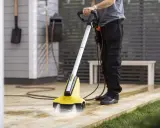 Person använder en gul borstmaskin för att slipa altanen. Vatten sprutar från borsten.