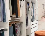 En walk-in closet med kläder på galgar, lådor och en blåvit klänning på väggen.