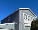 Blå himmel över ett gråblått trähus. Snart dags att måla fasad för att skydda det mot väder och vind.