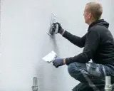 Man putsar en vit fasad med en bredspackel. Det är viktigt att man målar putsad fasad för att skydda den.
