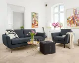En modern soffgrupp 3+2 i mörkblått tyg, med en fåtölj, soffbord, pall och konst på väggarna.