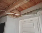Taket och väggarna är under renovering. Man ser träbjälkar och isolering. För att kunna måla ordentligt har man valt att ta bort lister vid målning.