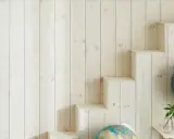 En vägg med ljus träpanel ger en mysig känsla. En gammal sjökarta hänger på ena sidan, medan en trappliknande hylla på andra sidan visar upp jordglober och böcker. Perfekt panel inomhus inspiration för äventyrliga själar.