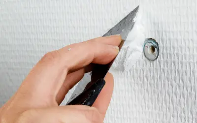 Hand spacklar ett hål i en vit, strukturerad vägg med en spackel.