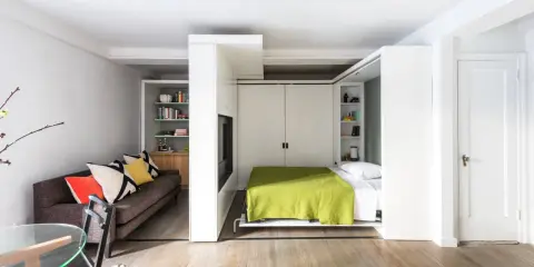 En modern lägenhet med smarta lösningar. En bekväm soffa i vardagsrumsdelen och en inbäddad säng med grön filt i sovrummet.