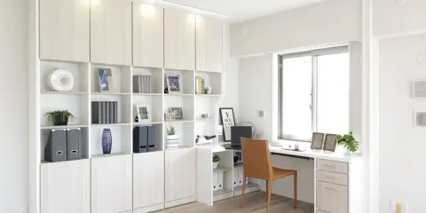 En djup bokhylla med många fack, dekorerad med böcker, vaser och foton. Bredvid finns ett skrivbord med en dator och en bekväm stol.