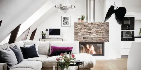 Mysigt vardagsrum med öppen spis, soffa och ett soffbord i 3 delar med blommor och ljus.