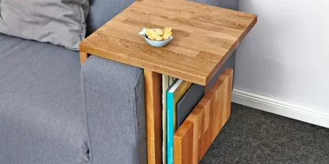Ett smart diy soffbord i trä som hängs över armstödet på en grå soffa. Perfekt för att förvara böcker och ha en skål med kex nära till hands.