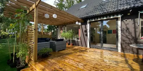 Träaltan med pergola och loungegrupp ger härlig altan inspiration. Solrosor och grönska ramar in.