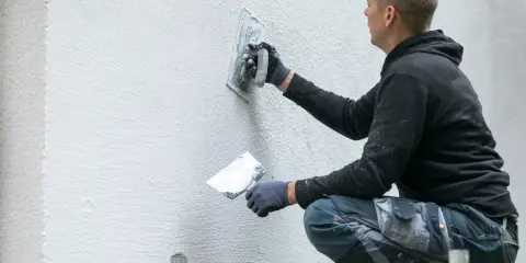 Man putsar en vit fasad med en bredspackel. Det är viktigt att man målar putsad fasad för att skydda den.